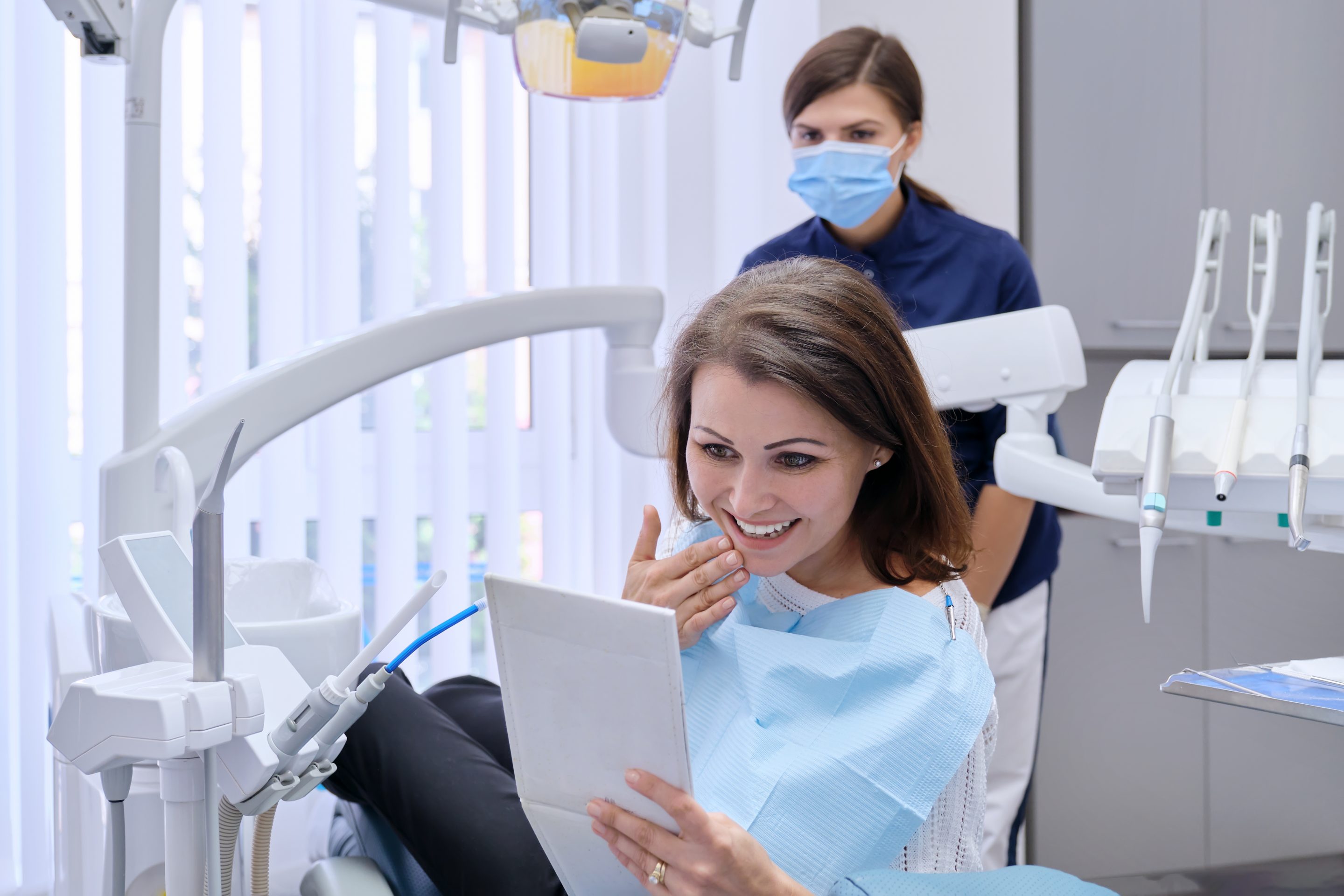 Expert Dental implant services in Rancho Santa Margarita. Smiling woman admiring new dental implants in mirror in dentist's chair.