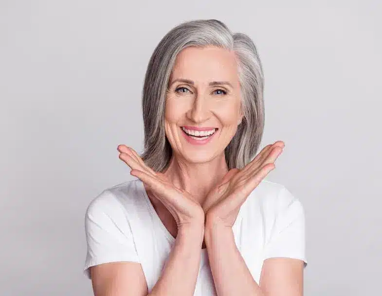 Smiling person with gray hair and hands raised.