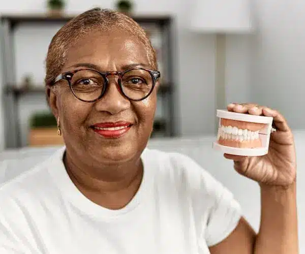 Smiling woman holding dentures in living room.