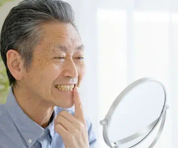 Senior man examining teeth in mirror, smiling.