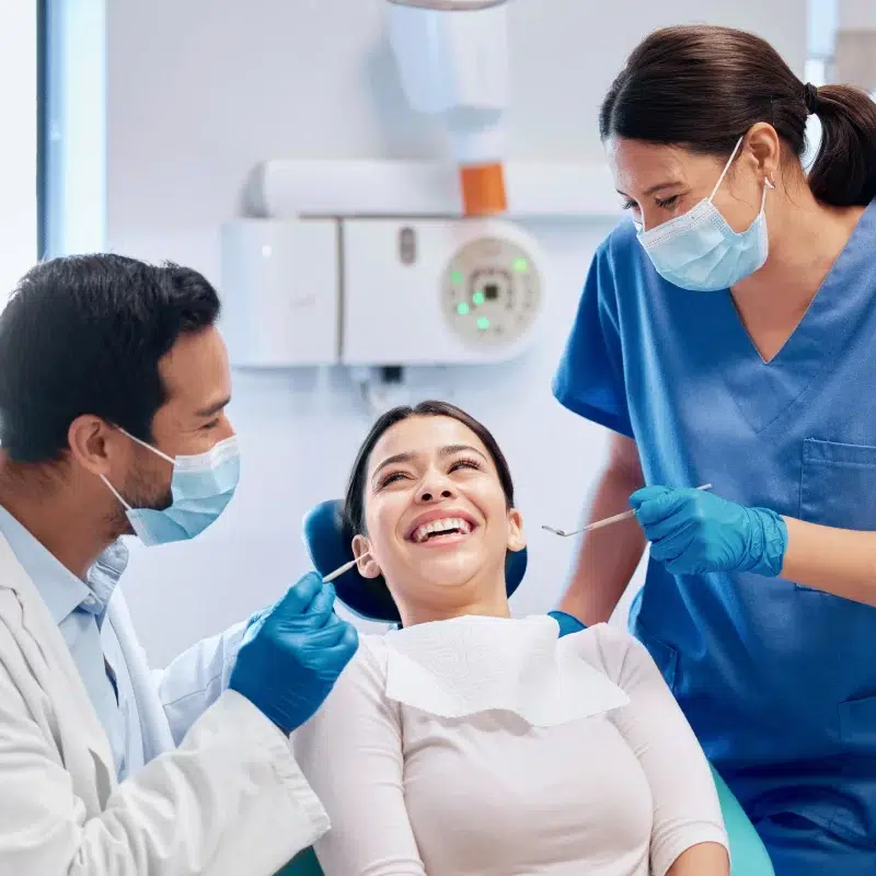 Dentists examining smiling patient in orthodontics appointment.