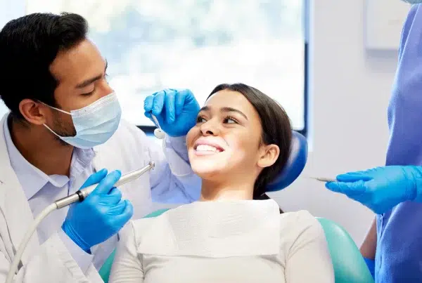 Dentist examining smiling patients teeth at clinic.