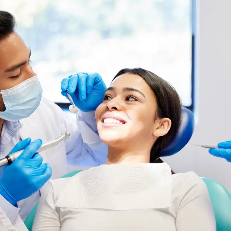 Dentist examining smiling patients teeth at clinic.