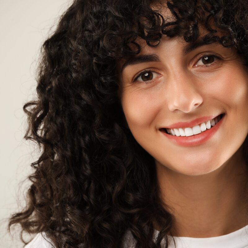 Woman smiling with curly hair against plain background.