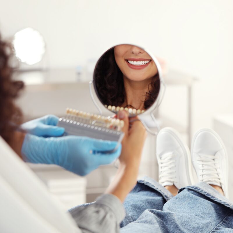 Dentist showing smile in mirror with shade guide.